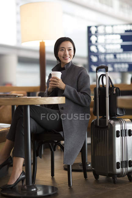 Азиатка ждет в аэропорту с кофе — стоковое фото