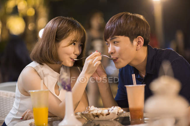 Young Chinese couple feeding each other ice cream in cafe — Stock Photo