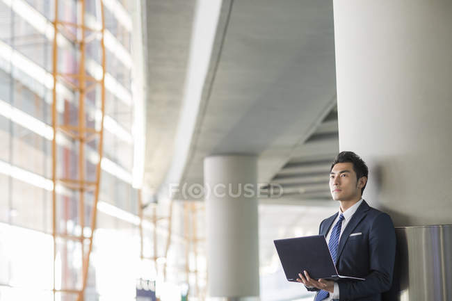 Китайский бизнесмен стоит с ноутбуком в помещении — стоковое фото