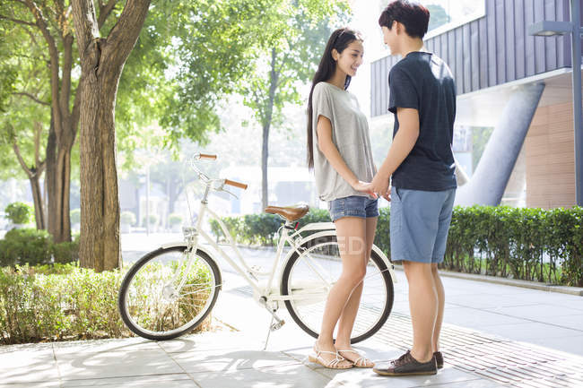 Coppia cinese che si tiene per mano nel campus con la bicicletta — Foto stock