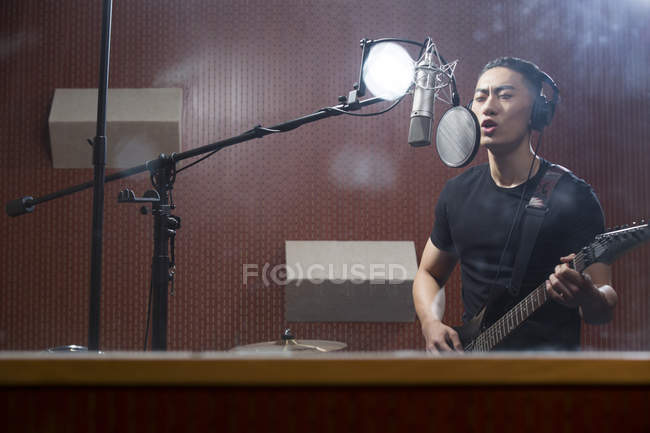 Homem chinês cantando com guitarra em estúdio de gravação — Fotografia de Stock