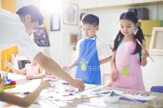Niños chinos pintando en clase de arte con maestro - foto de stock