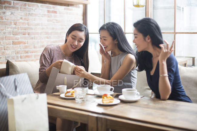 Chinese woman demonstrating new clothing to female friends in coffee shop — Stock Photo