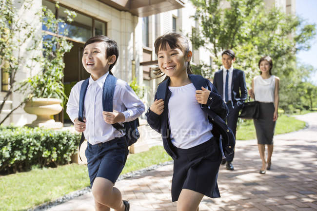 Chinese sister and brother with backpacks running on street with parents — Stock Photo