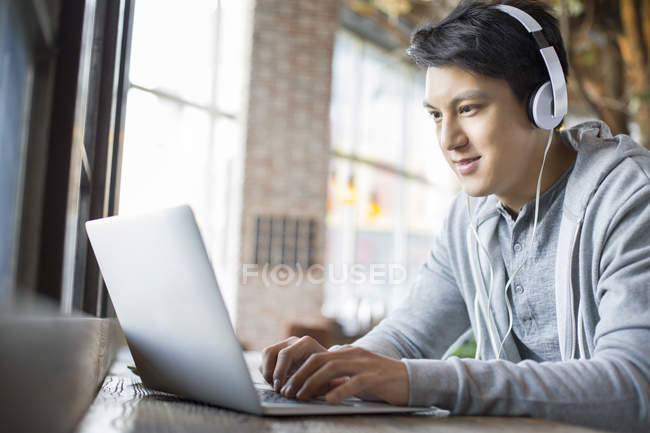 Китаєць в навушниках, використовуючи ноутбук у кафе — стокове фото