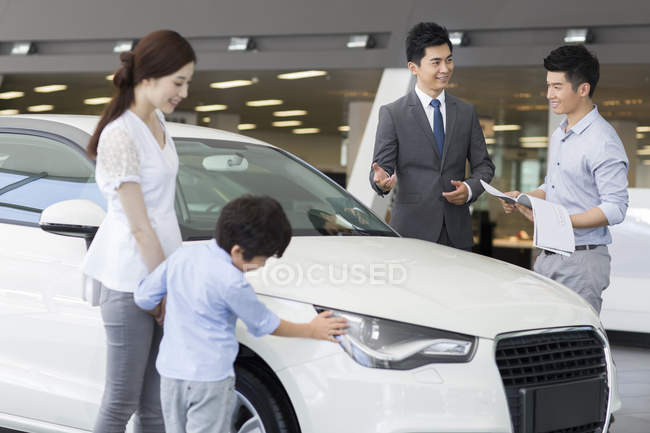 Chinese family examining new car in showroom with car seller — Stock Photo