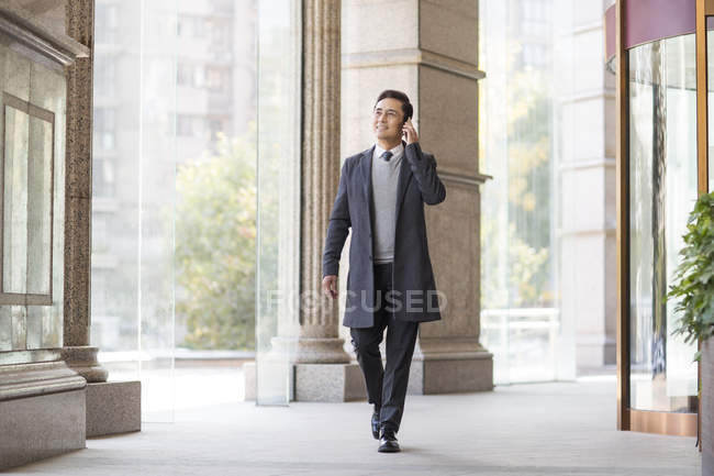 Chinese businessman walking and talking on phone in city — Stock Photo