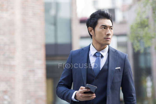 Азиатский мужчина держит смартфон на городской улице — стоковое фото