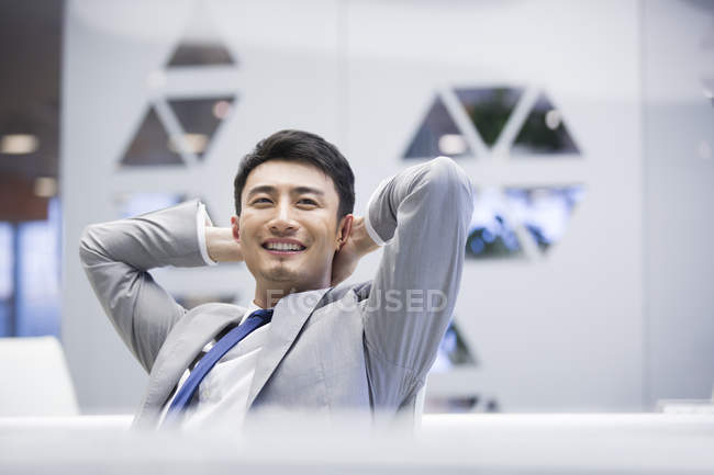 Chinese businessman sitting with hands behind head in office — Stock Photo