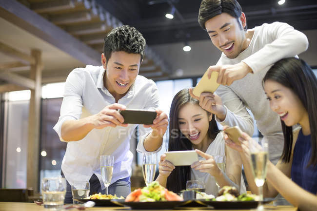Amigos asiáticos tirando fotos de comida enquanto jantam no restaurante — Fotografia de Stock