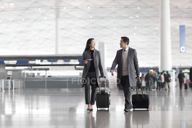 Uomini d'affari cinesi che tirano bagagli a ruote nella hall dell'aeroporto — Foto stock