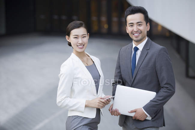 Asiático gente de negocios de pie en la calle con gadgets y sonriendo - foto de stock
