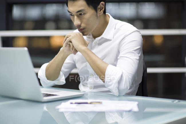 Pensive Chinese businessman sitting at office desk with hands clasped — Stock Photo