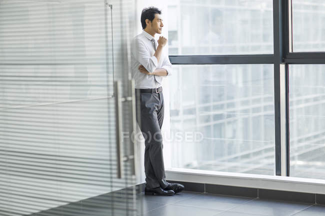 Chinese businessman thinking and looking through window in office — Stock Photo