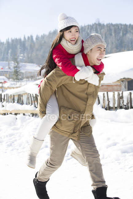 Chinês homem dando namorada piggyback no neve aldeia — Fotografia de Stock