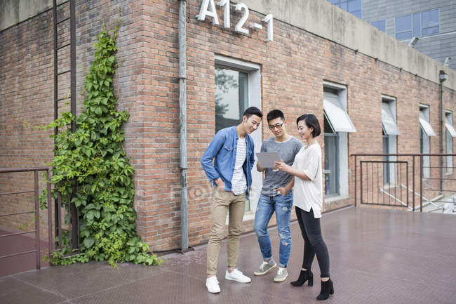 Equipo de negocios casual chino hablando con tableta digital en la ciudad - foto de stock