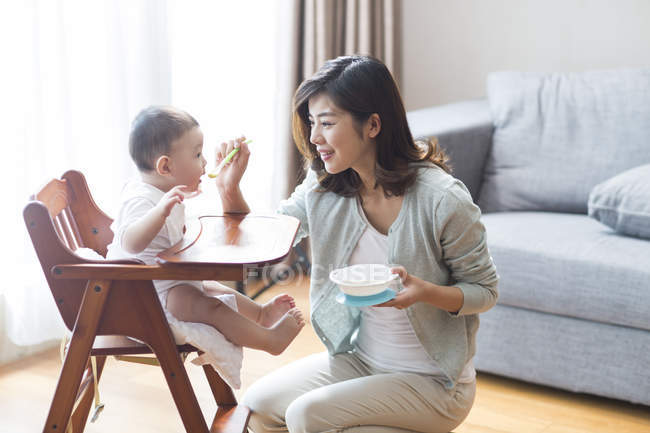 Mère chinoise nourrissant bébé garçon en chaise haute — Photo de stock