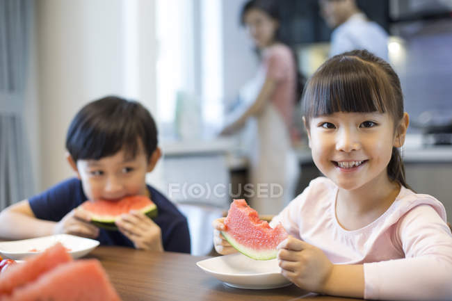 Irmãos chineses comendo melancia na mesa da cozinha — Fotografia de Stock
