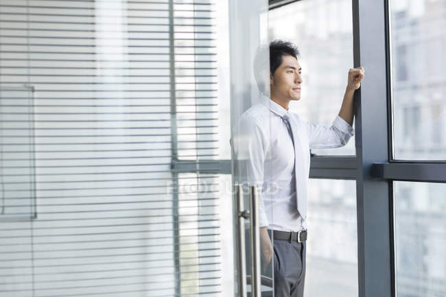 Chinesischer Geschäftsmann lehnt sich an Tür und schaut durch Fenster — Stockfoto