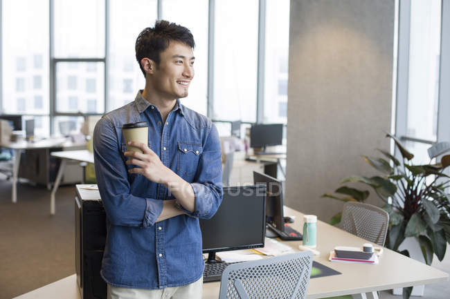 Young Chinese man taking coffee break in office — Stock Photo