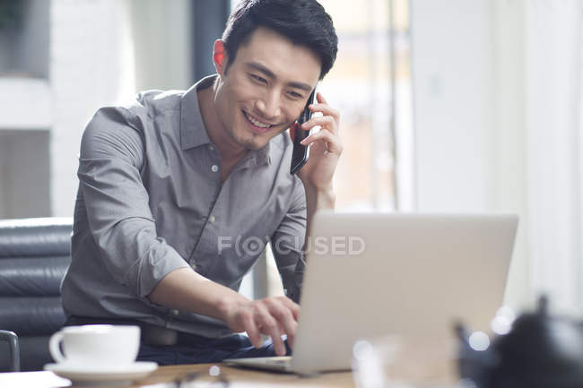 Asian man talking on phone in office — Stock Photo