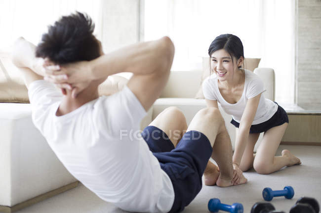 Donna cinese che aiuta l'uomo a fare sit-up a casa — Foto stock