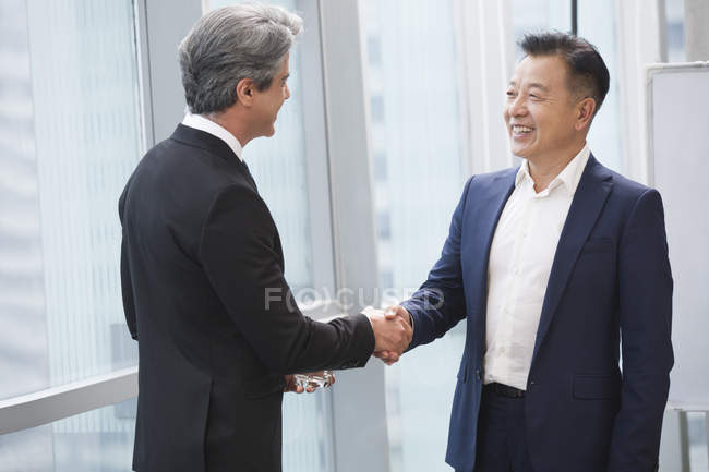 Businessmen shaking hands in meeting room — Stock Photo