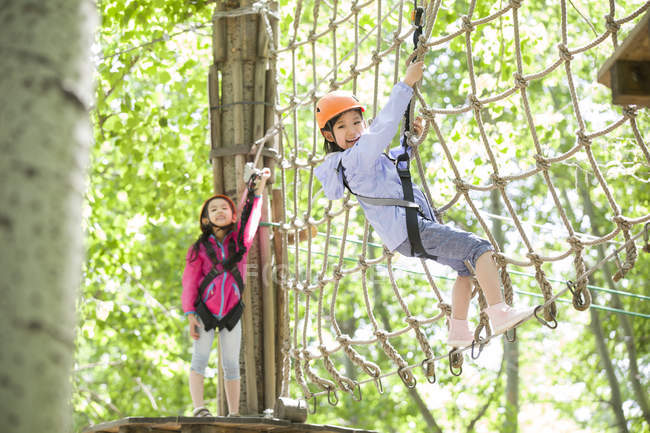 Chinese girls climbing on net in tree top adventure park — Stock Photo