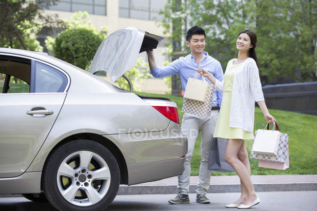 Chinese couple taking shopping bags from car trunk — Stock Photo