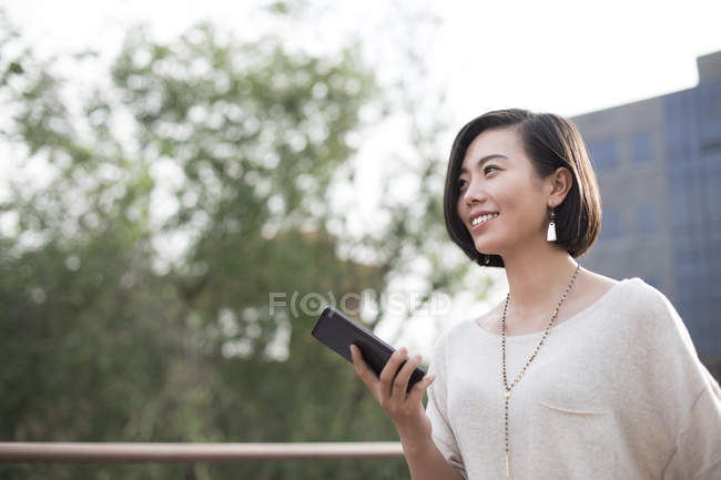 Chinese woman holding smartphone in city — Stock Photo