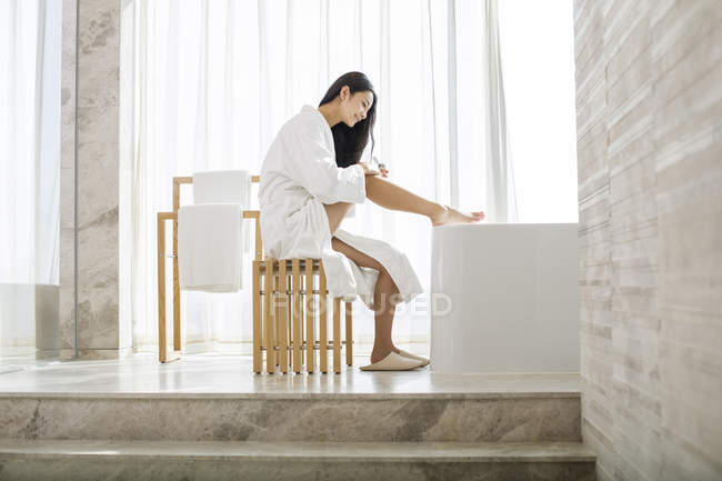 Chinese woman applying moisturizer to legs — Stock Photo