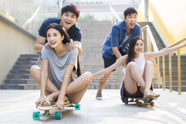 Chinese men pushing girlfriends on skateboards — Stock Photo