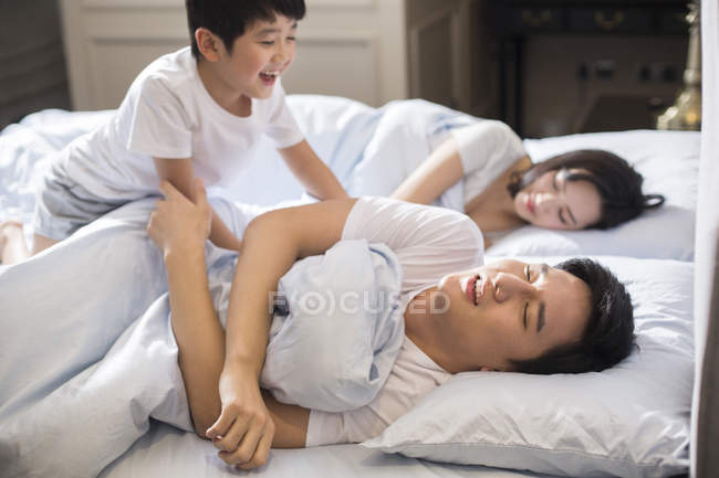 Chinese boy waking up parents in bedroom — Stock Photo