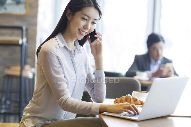 Азиатка разговаривает по телефону в кафе — стоковое фото