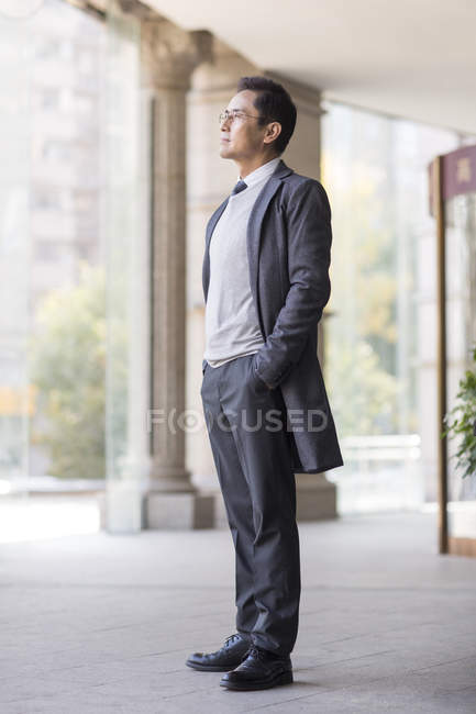 Китайський бізнесмен з руки в кишені, фотографіях хтось дивитися вбік в місті — стокове фото