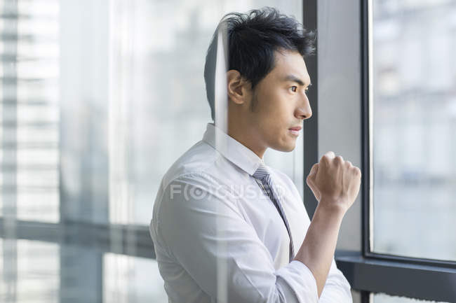 Китайський бізнесмен, дивлячись через вікно в офісі — стокове фото