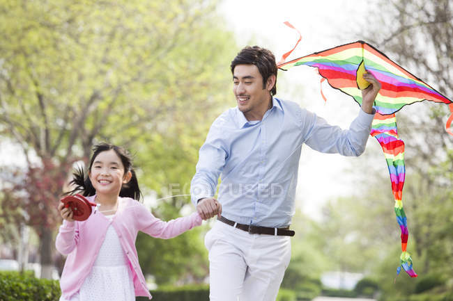 Asian father and daughter flying kite in city park — Stock Photo