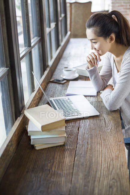 Mujer china usando el ordenador portátil mientras estudia en la cafetería - foto de stock