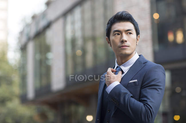 Азиатский мужчина выпрямляет галстук на улице — стоковое фото