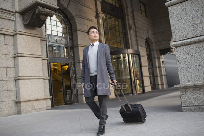 Chinese businessman pulling wheeled luggage in city — Stock Photo