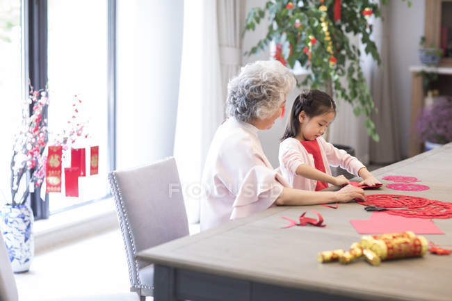 Nieta y abuela haciendo chino Año Nuevo papel-corte - foto de stock