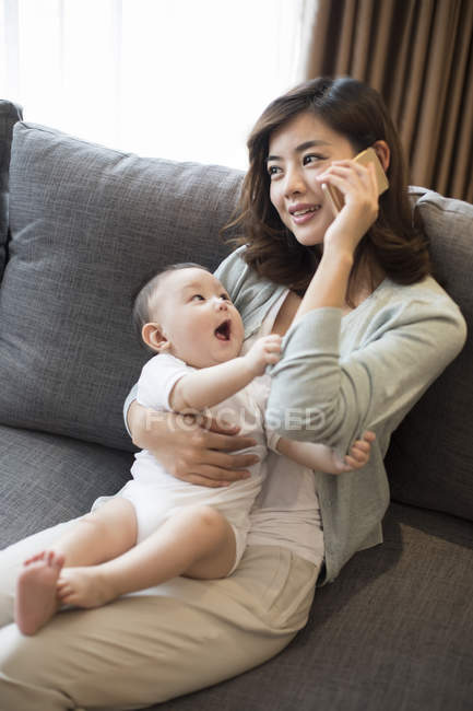 Chinese baby boy looking at mother talking on phone with mouth open — Stock Photo