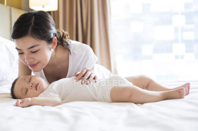 Madre china chequeando durmiendo bebé niño en la cama - foto de stock