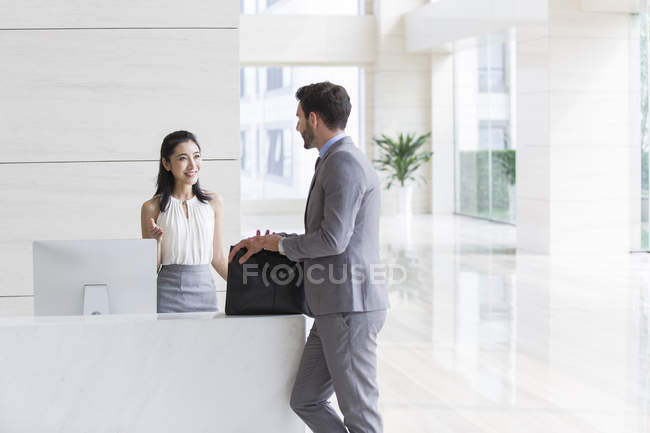 Empresario hablando con recepcionista en edificio de oficinas - foto de stock