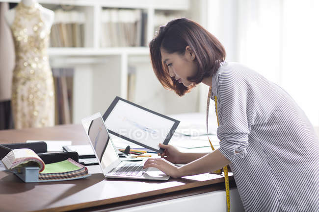 Designer de moda feminina trabalhando em estúdio com laptop — Fotografia de Stock