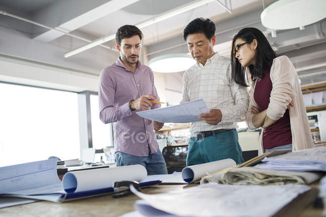 Архитекторы держат и обсуждают чертежи в офисе — стоковое фото