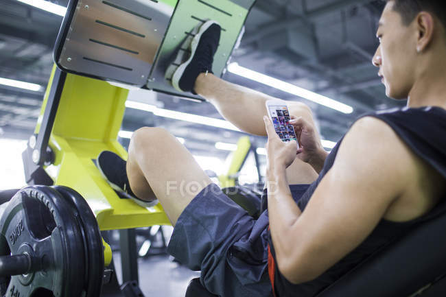 Asiatischer Mann benutzt Telefon auf Trainingsgerät — Stockfoto