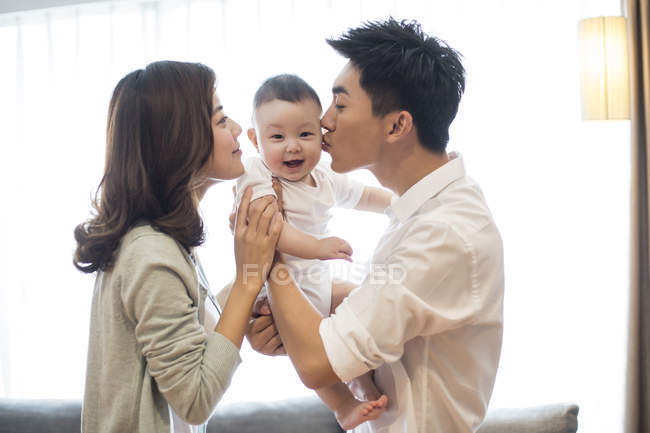 Padres chinos besando al niño en las mejillas - foto de stock