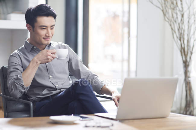 Hombre asiático trabajando con el ordenador portátil y café en la oficina - foto de stock