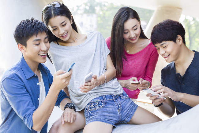 Китайские друзья смотрят на смартфоны на улице — стоковое фото